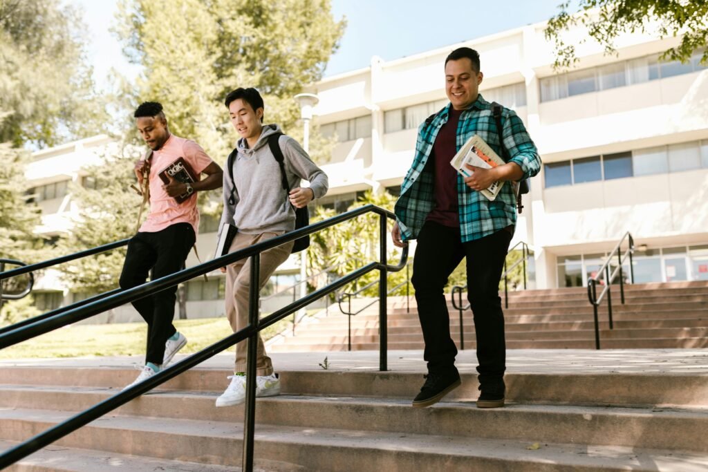 Three college students with backpacks and books on campus stairs outdoors.
